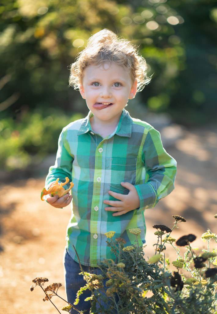A young boy in a green plaid shirt is holding a toy dinosaur in Huntington Beach Park.