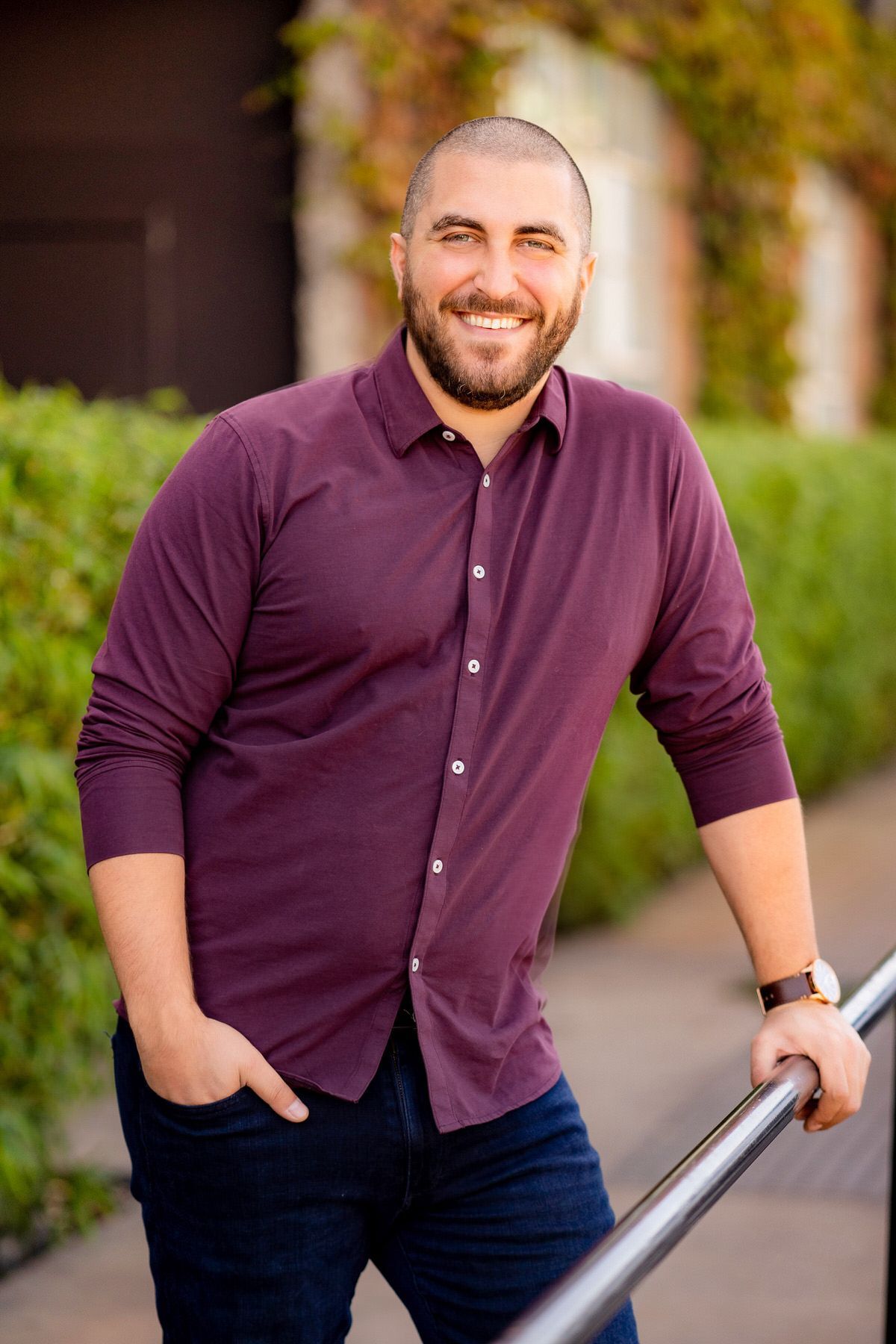 A man in a purple shirt is standing next to a railing for a headshot