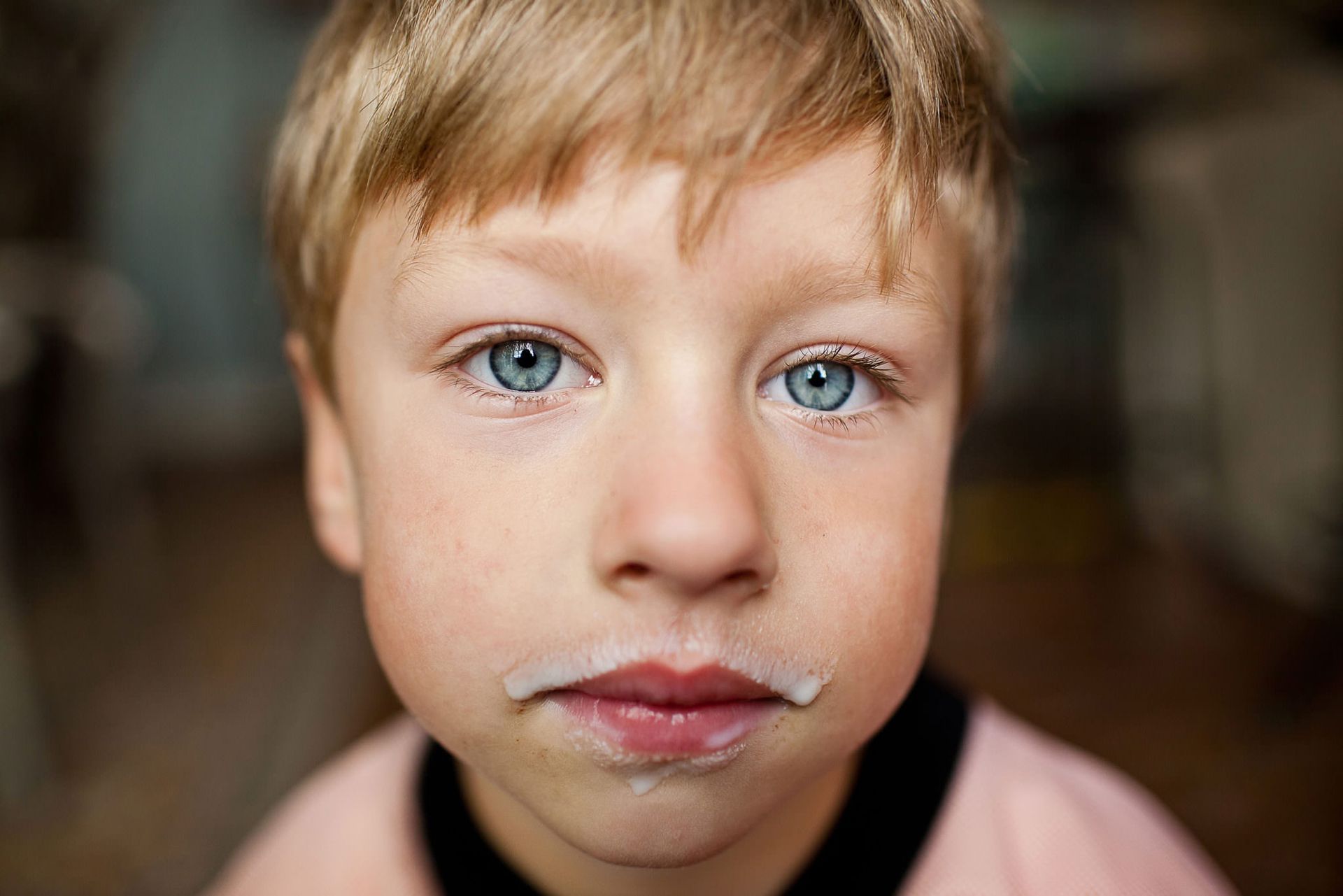 A young boy is making a funny face with milk on his face.