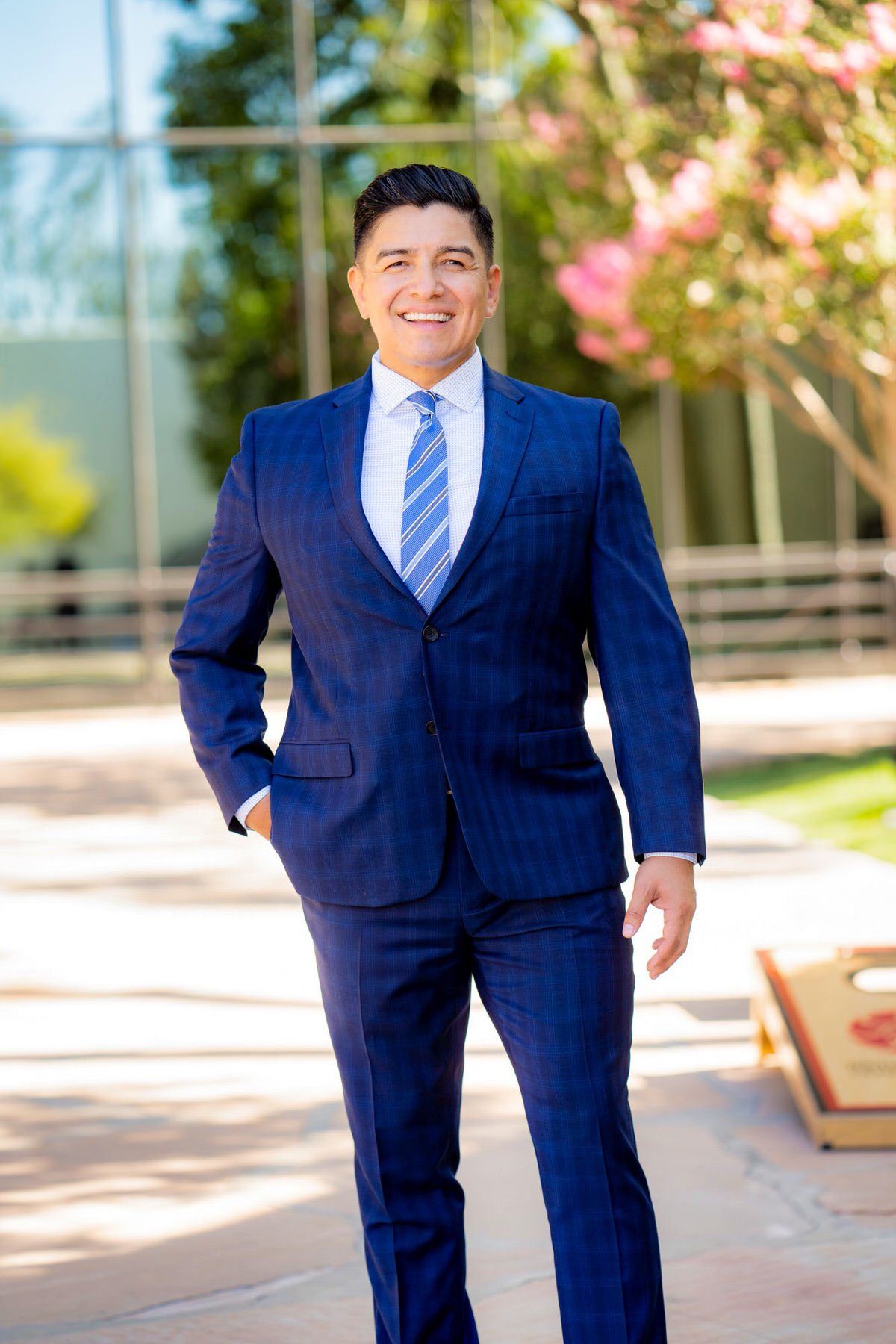 A man in a blue suit and tie is standing in front of a building for a LinkedIn photo