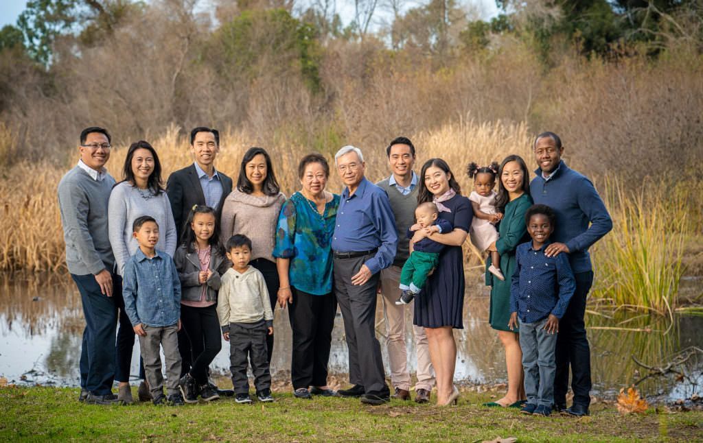 A large family is posing for a picture in front of a pond at Huntington Central Park California.