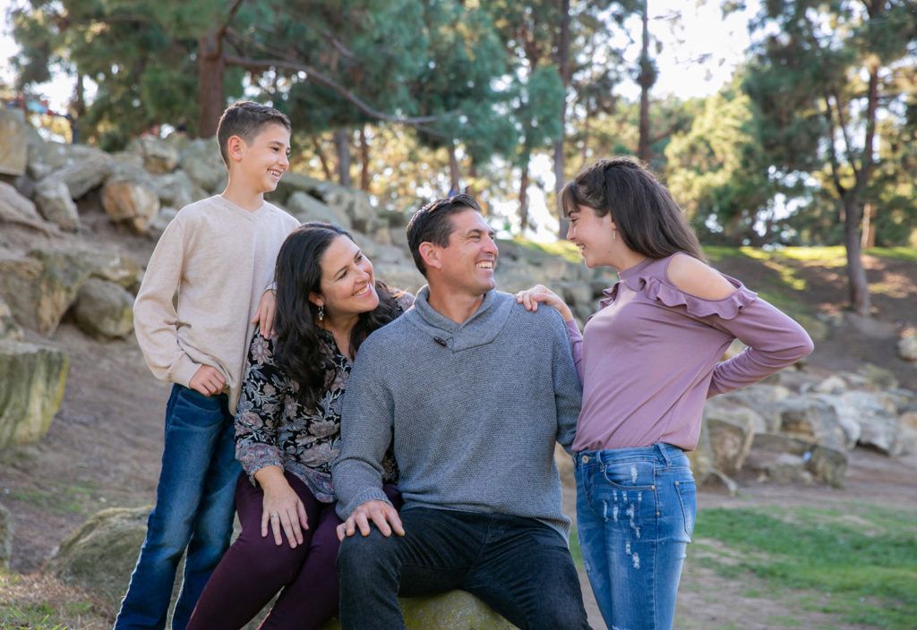 A family is posing for a picture while sitting on a rock inTewinkle Park in Costa Mesa