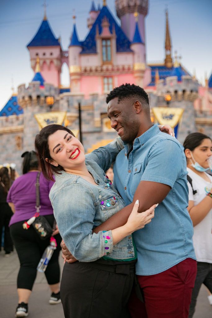 A man and a woman are hugging in front of a castle at disneyland.