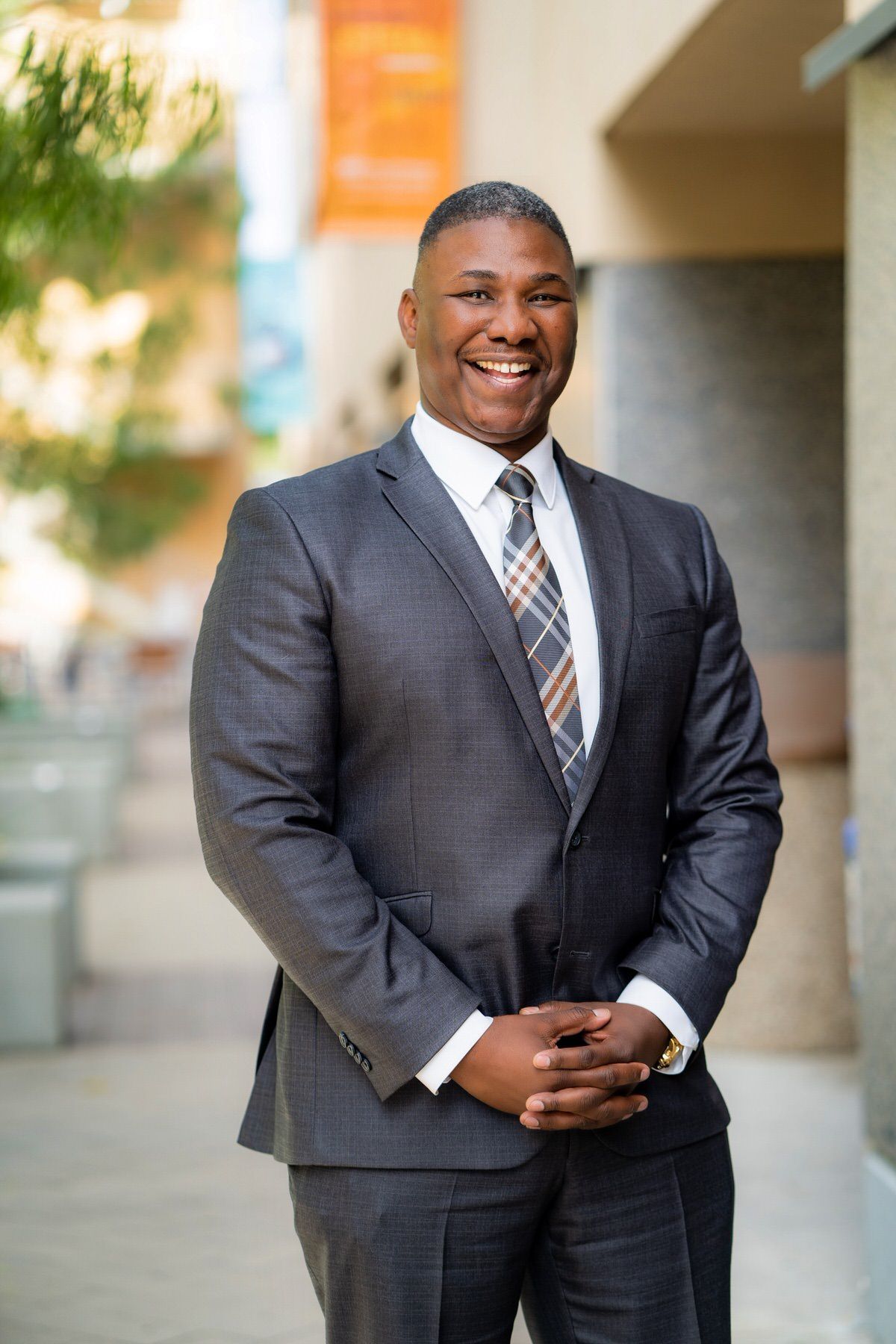 A man in a suit and tie is standing on a sidewalk with his hands folded.