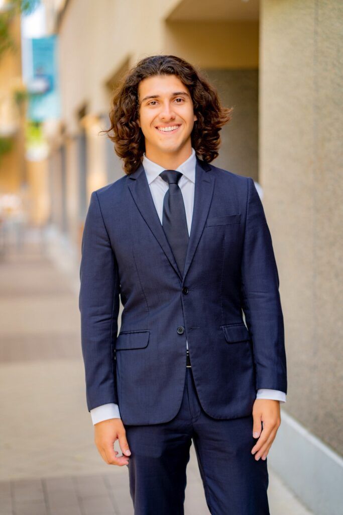 A young man in a suit and tie is standing in front of a building.
