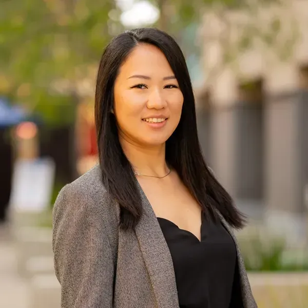 A woman wearing a gray jacket and a black top is smiling for the camera.