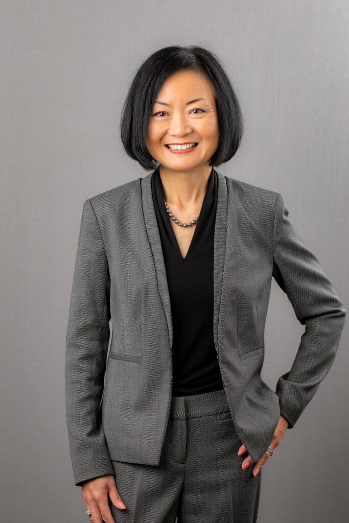 A woman in a suit is smiling and standing with her hands on her hips.