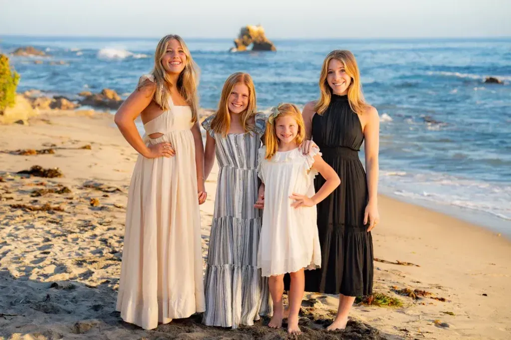 Four sisters are posing for a picture on the beachwearing dresses