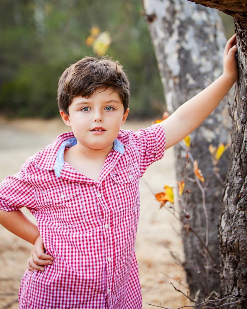 A young boy in a red shirt is leaning against a tree. In Irvine regional Park