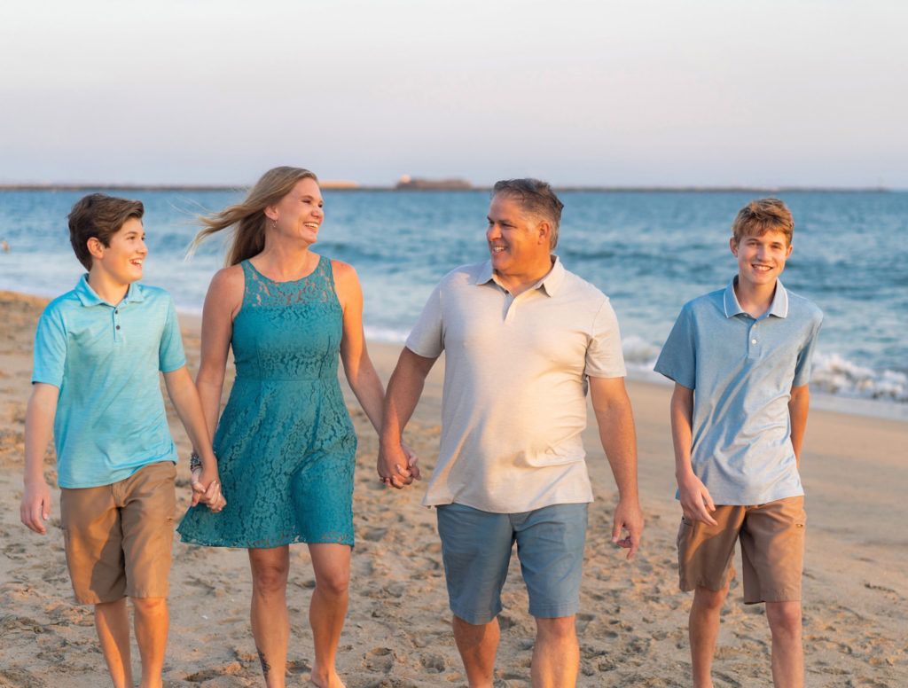 A family is walking on the beach holding hands.