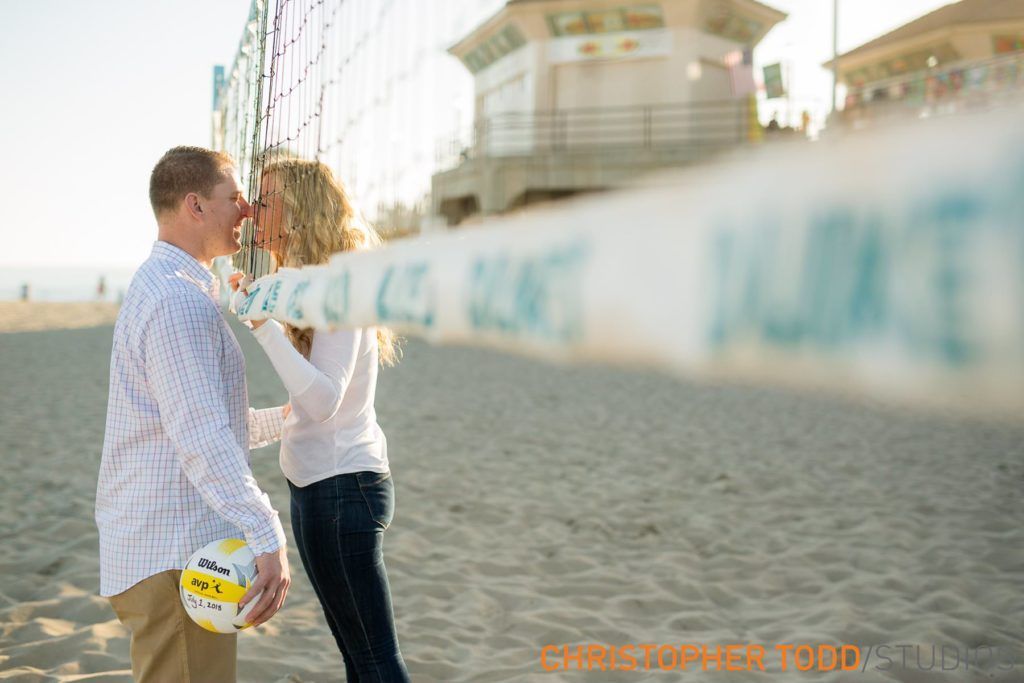A man and a woman are kissing on the beach while holding a volleyball at the Huntington Beach pier