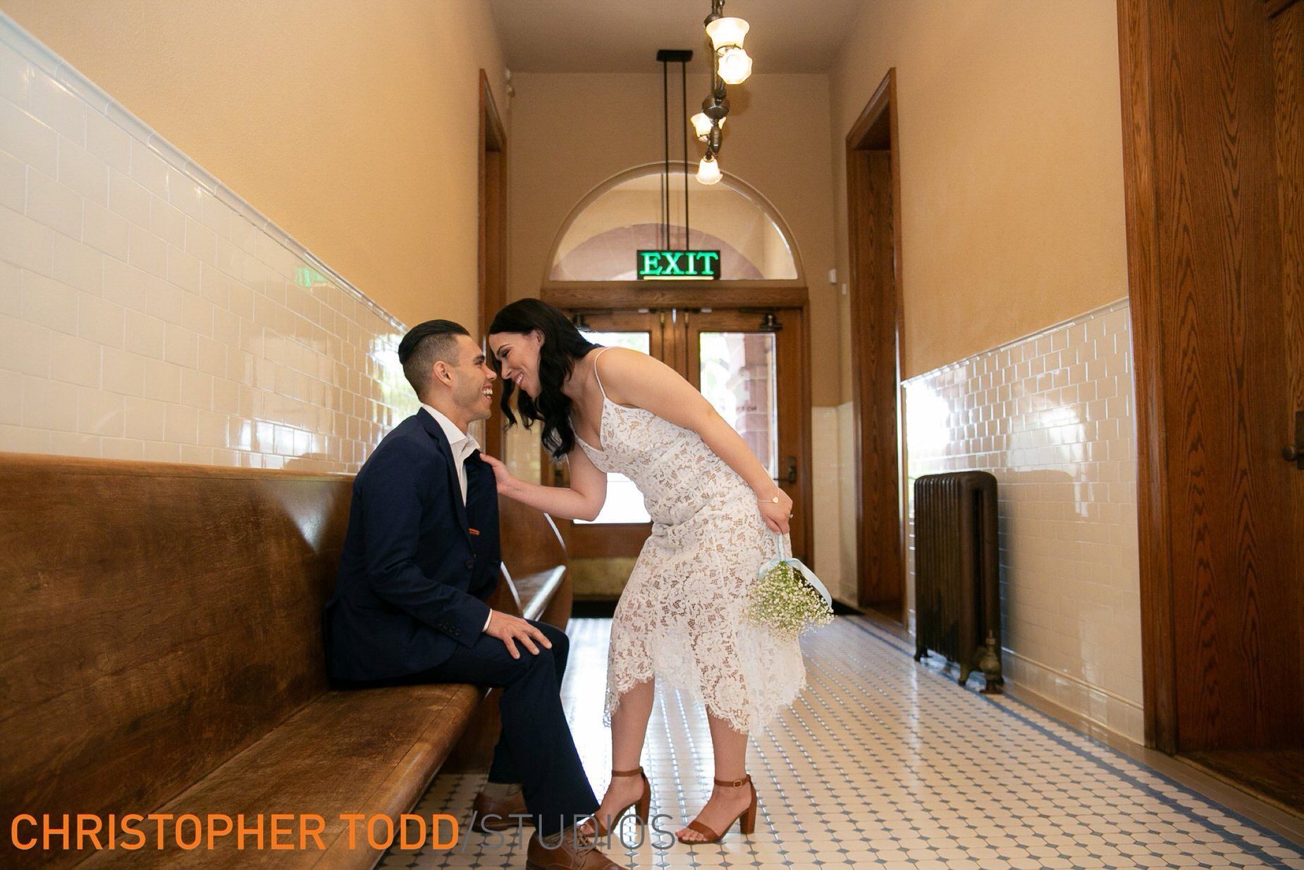 A bride and groom are sitting on a bench in a hallway at the Old Courthouse.