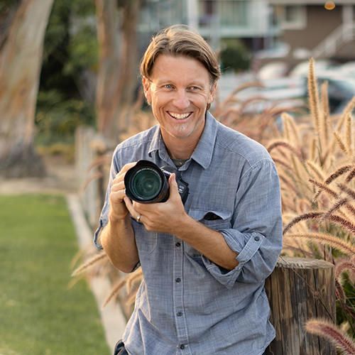 A man in a blue shirt is holding a camera and smiling.
