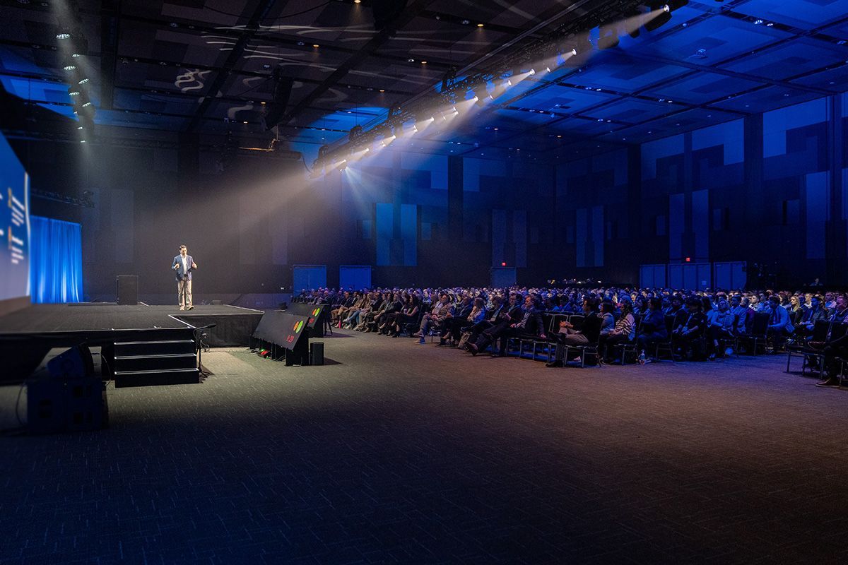A man is standing on a stage in front of a crowd at a conference.