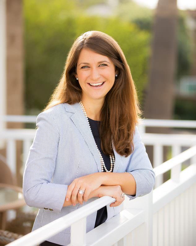 A woman in a striped jacket is leaning on a railing and smiling.