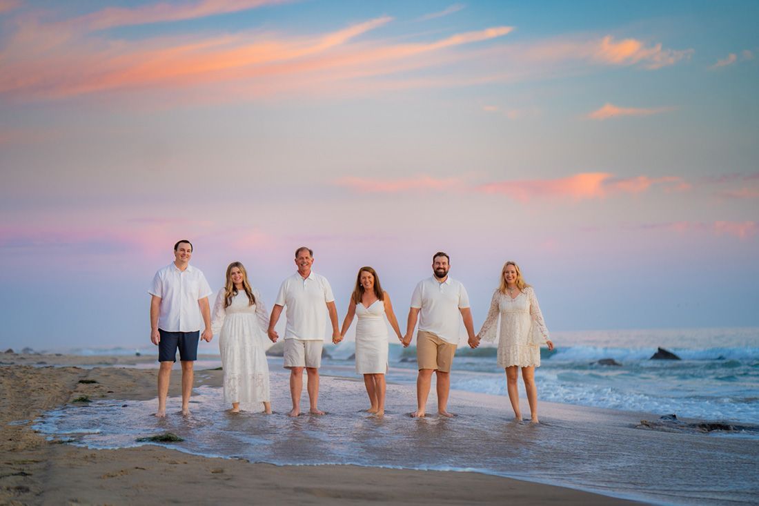 A group of people are standing on a beach holding hands during sunset. 