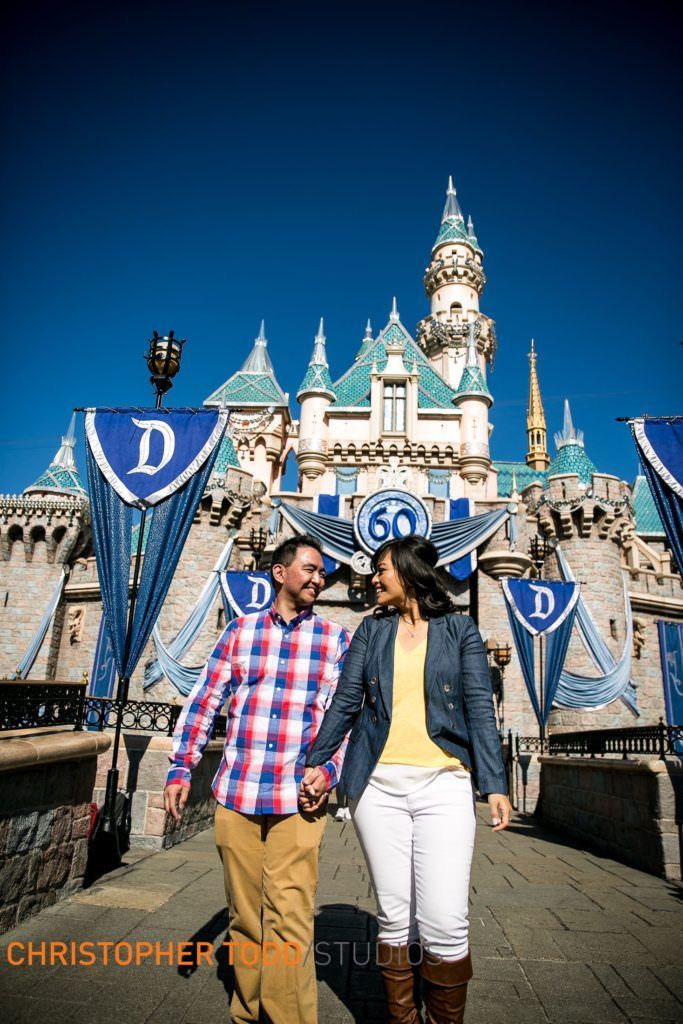 A man and a woman are holding hands in front of a castle at disneyland