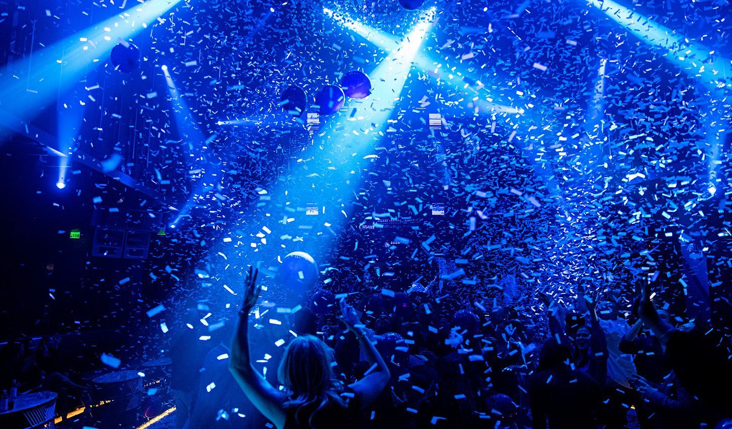 A crowd of people are dancing in a club with confetti falling from the ceiling.
