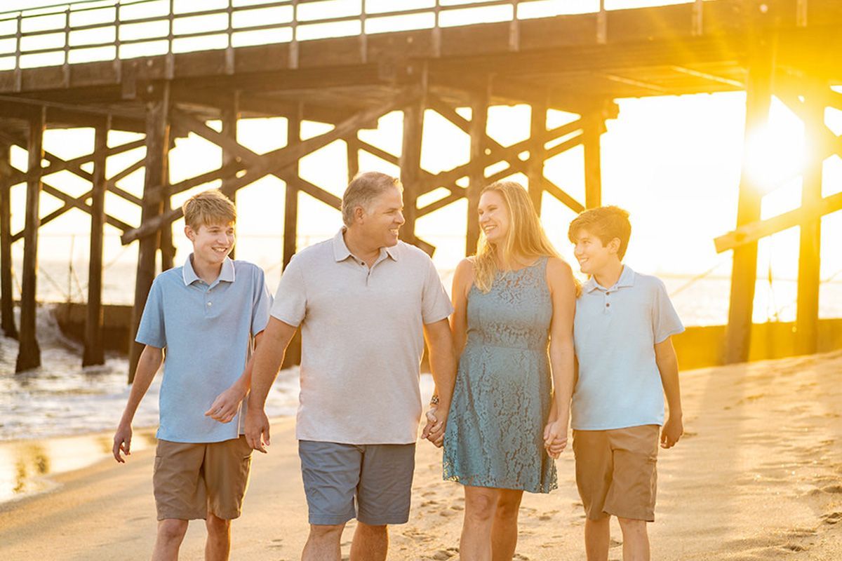 A family is walking on the beach at sunset holding hands.