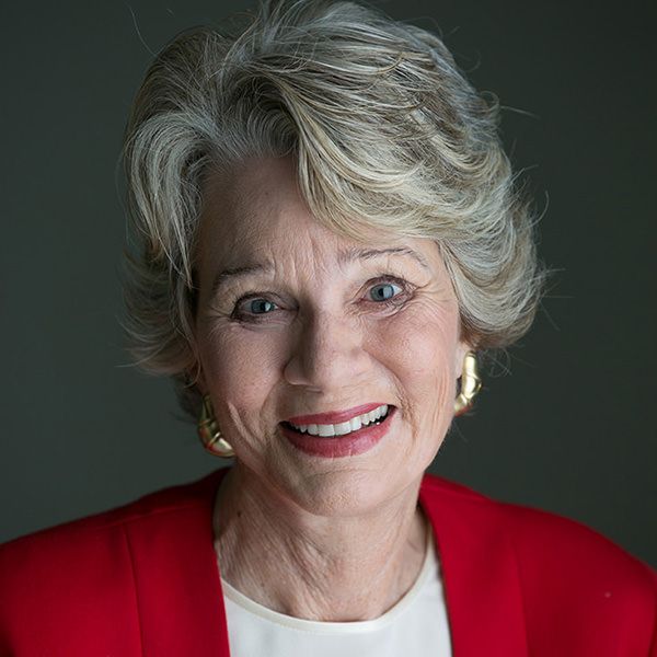 A woman wearing a red jacket and earrings is smiling for the camera.