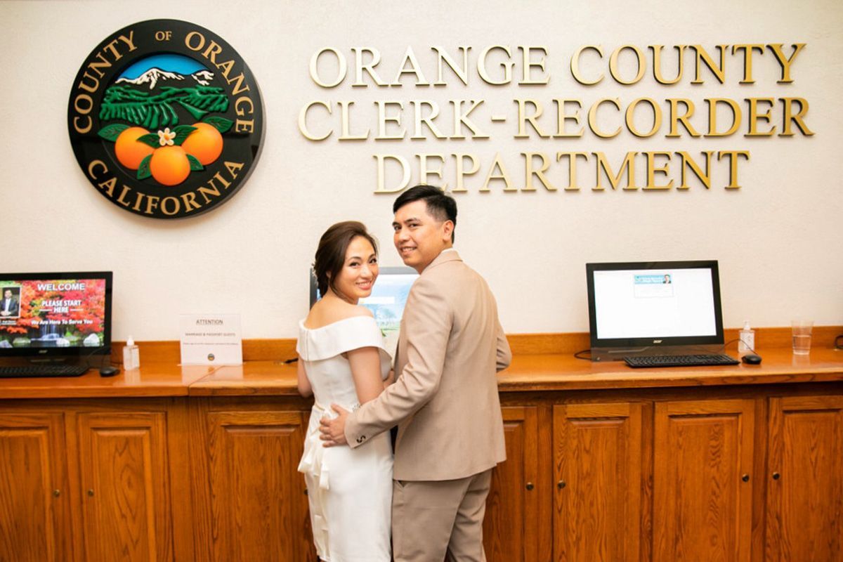 A bride and groom are posing for a picture in front of the orange county clerk recorder department.