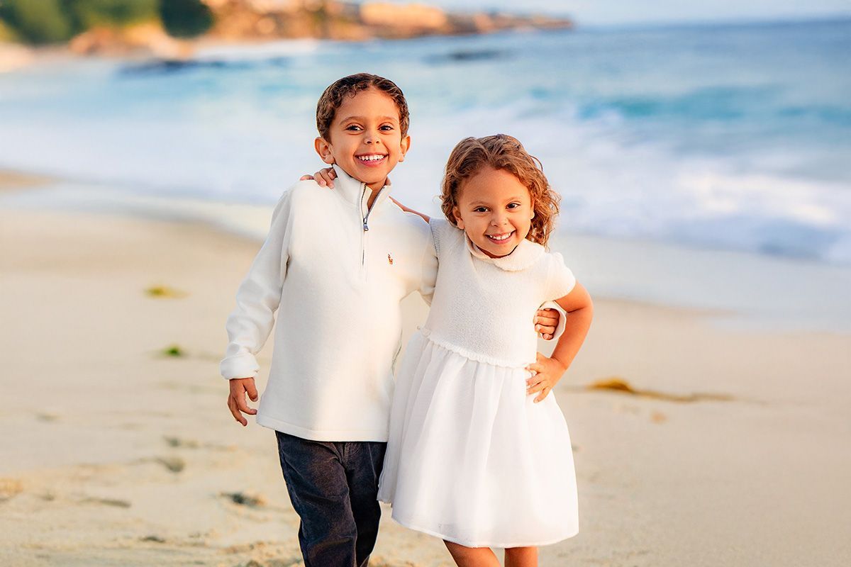 A boy and a girl are standing next to each other on the beach.