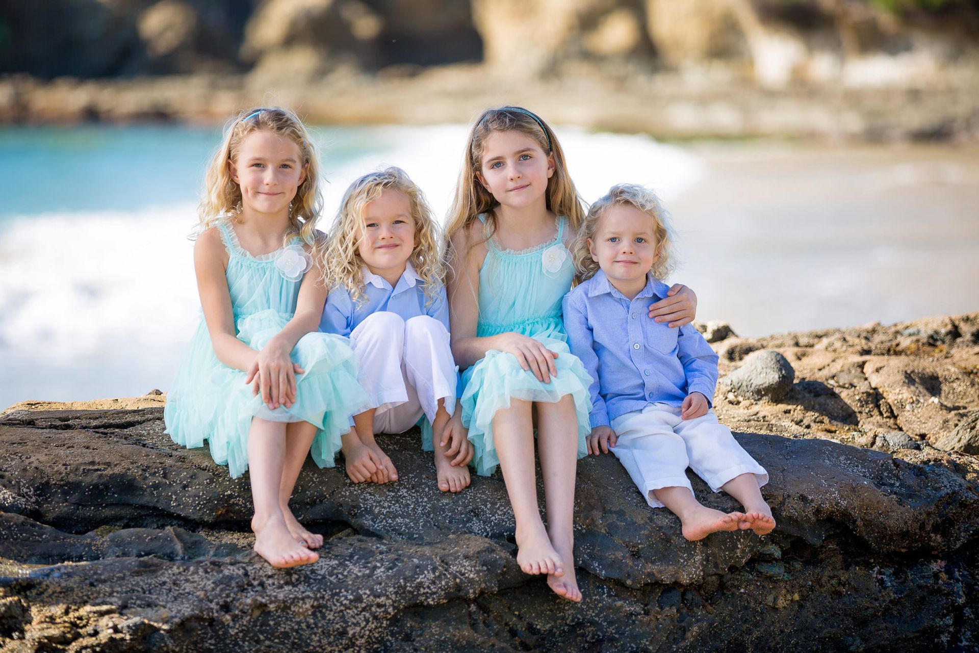 Outdoor Beach Family Photographer A group of children are sitting on a rock on the beach.