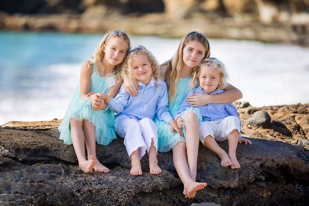 A group of children are sitting on a rock on the beach.
