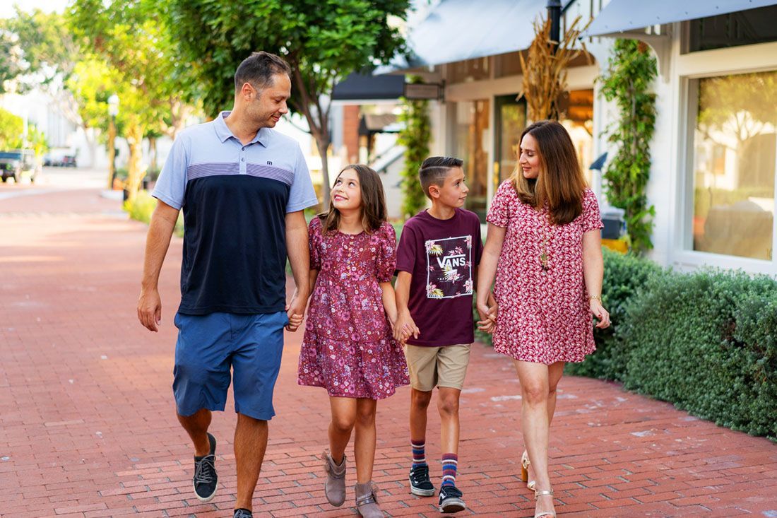 A family is walking down a brick sidewalk holding hands.