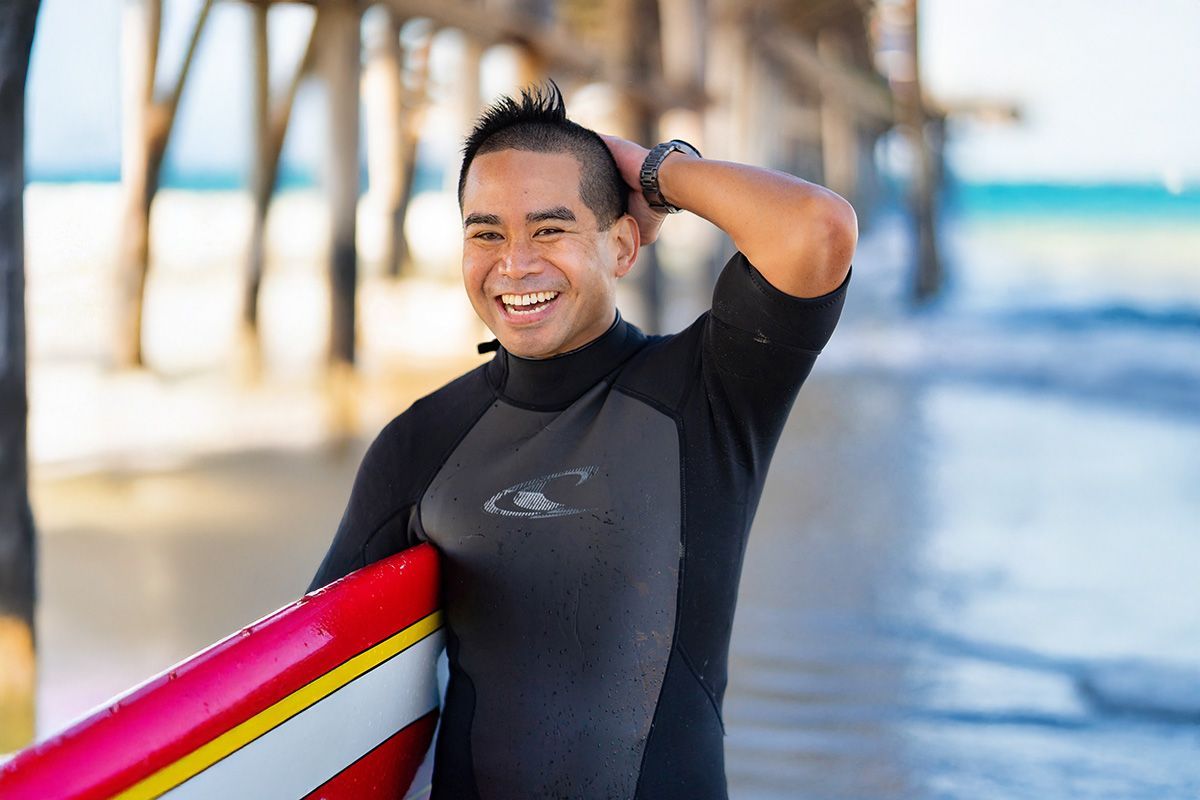 A man in a wetsuit is holding a surfboard on the beach.