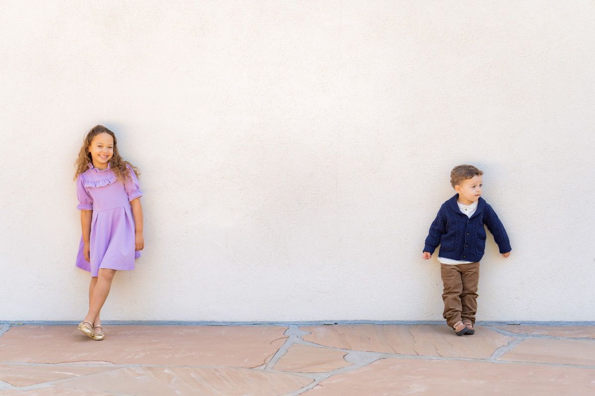 A boy and a girl are standing next to each other in front of a white wall in Naguch Garden in Costa Mesa. 