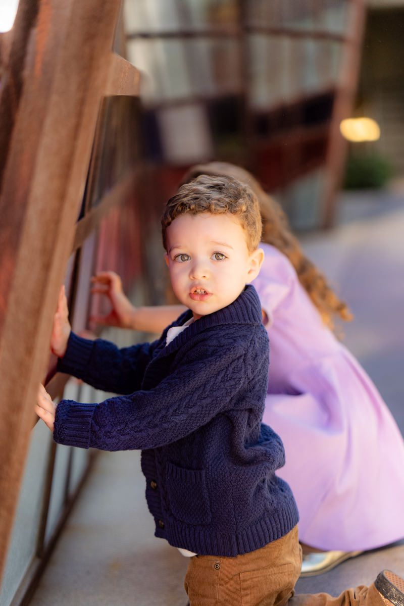 A little boy in a blue sweater is standing next to a girl in a purple dress at Noguchi gardens