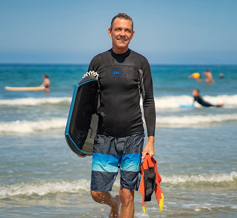 A man in a wetsuit is walking out of the ocean holding a surfboard.