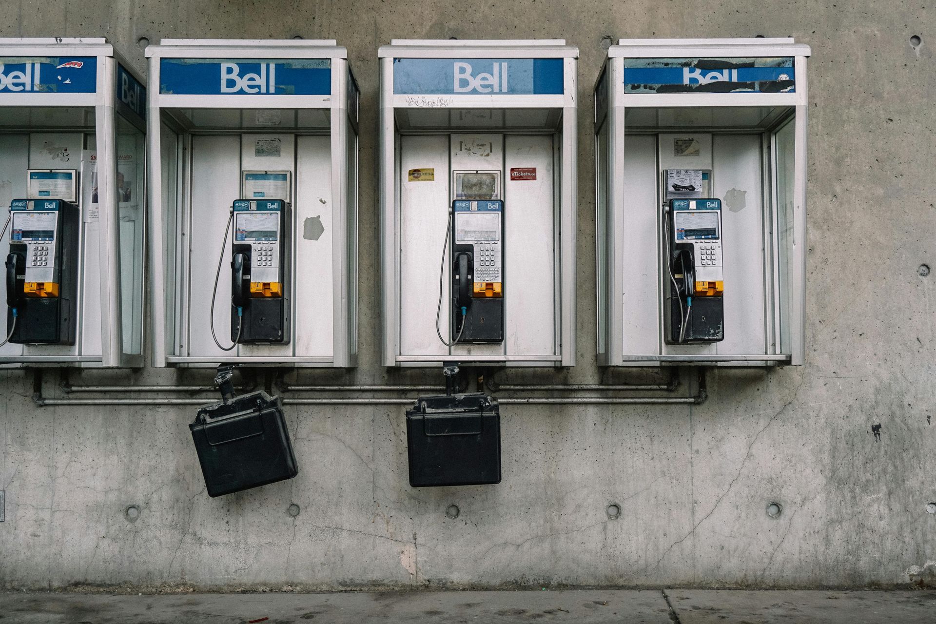 Four gray Bell public telephone booths mounted on a concrete wall, with two black boxes hanging beneath them.