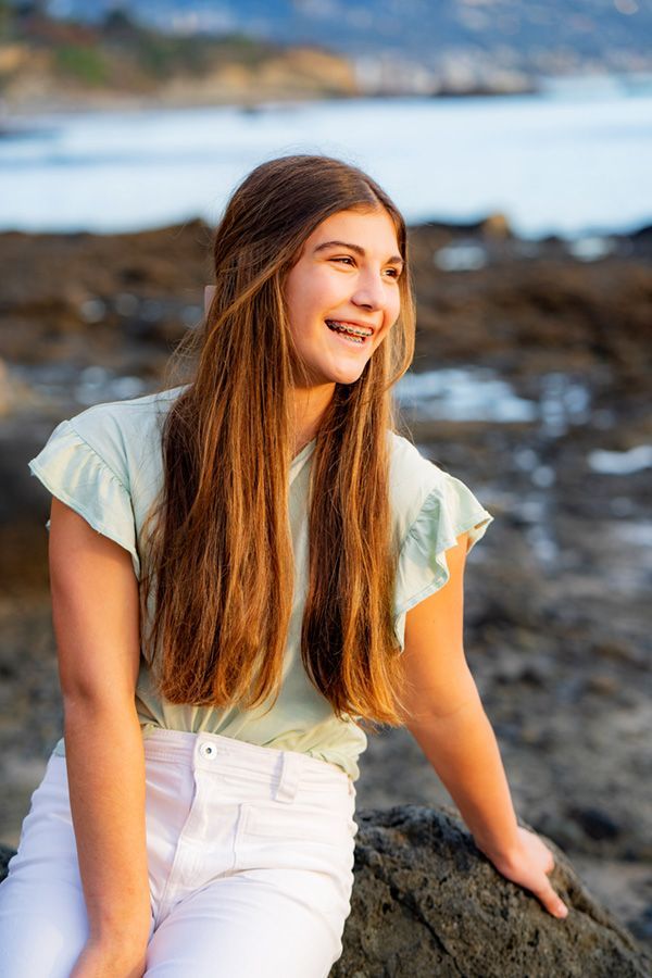 A young girl is sitting on a rock on the beach.