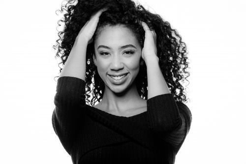 A black and white photo of a woman with curly hair holding her hair.
