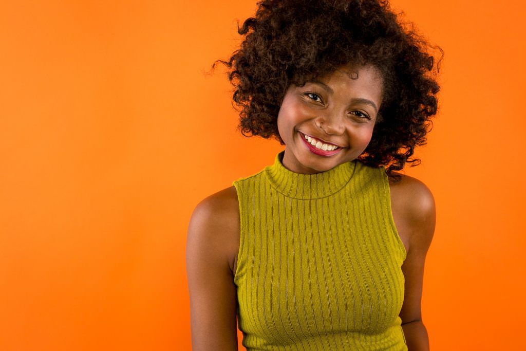 A woman with curly hair is smiling and wearing a yellow tank top for a different LinkedIn photo.