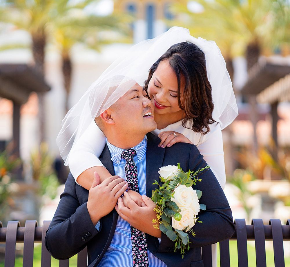 A bride and groom are posing for a picture on a bench.