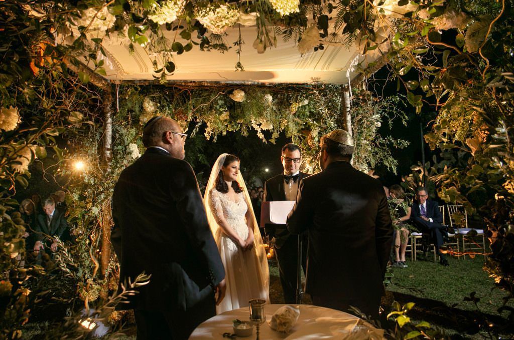 A bride and groom are standing under a Chupa at a wedding ceremony.