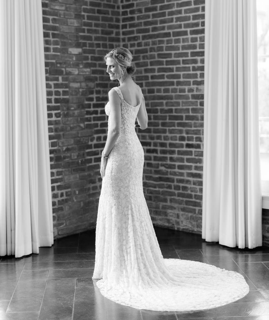 A black and white photo of a bride in a wedding dress standing in front of a brick wall.