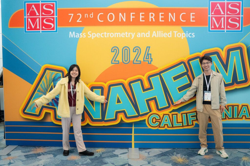 A man and a woman are standing in front of a large sign for the 72nd conference in anaheim california.