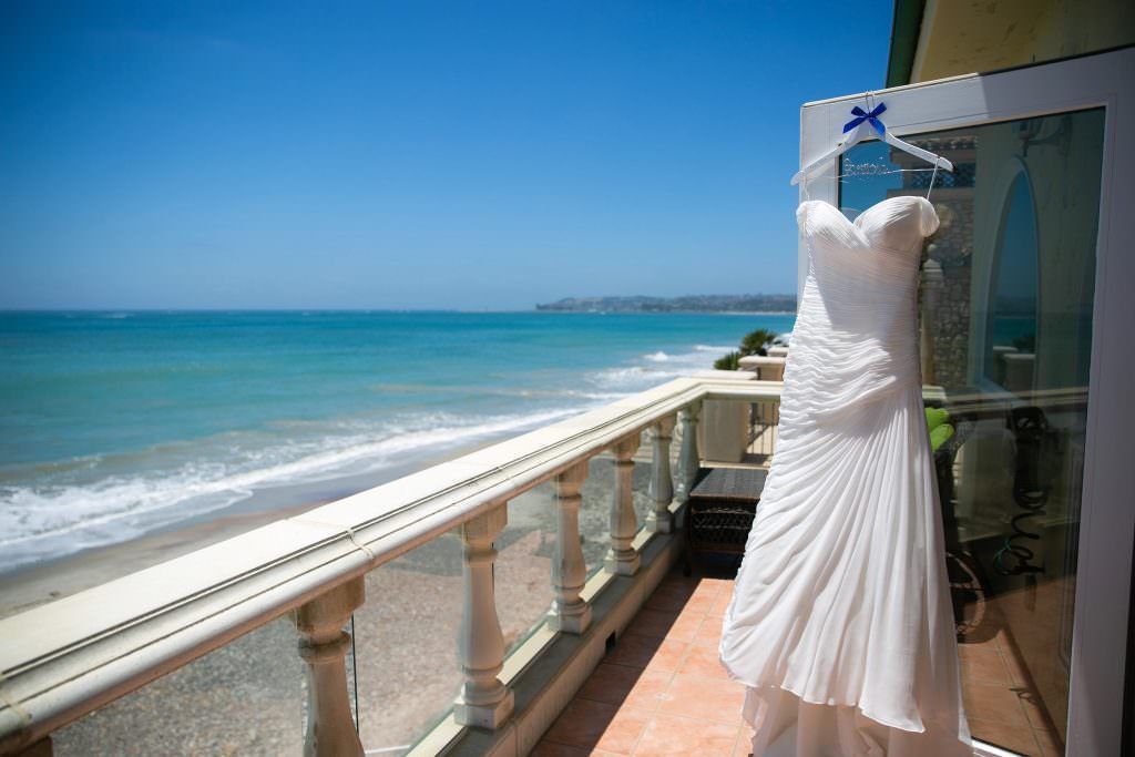 A wedding dress is hanging on a balcony overlooking the ocean.