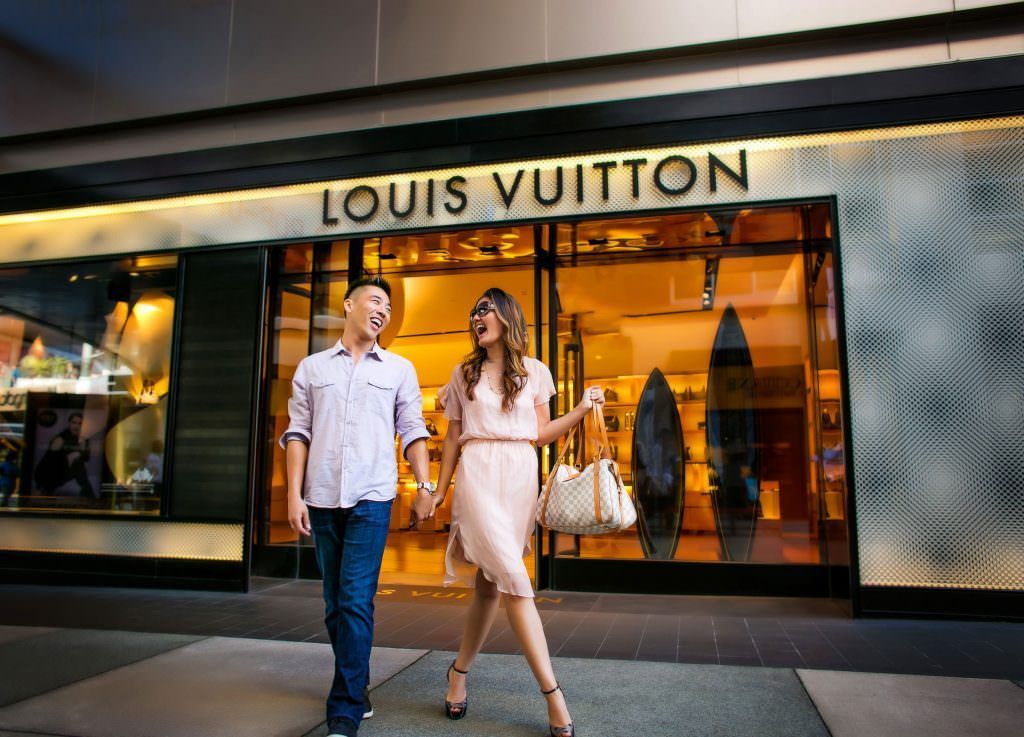 A fun engagement portrait of a couple walking in front of a louis vuitton store