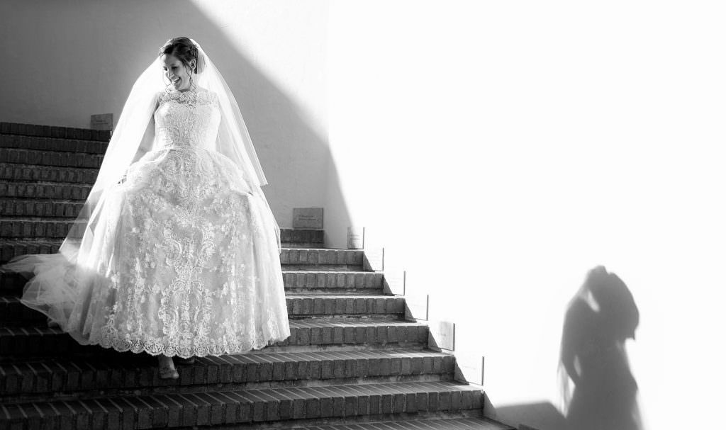 A bride in a wedding dress is standing on a set of stairs at the Bowers Museum in Santa Ana