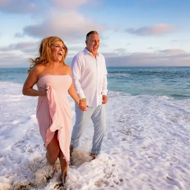 A man and a woman are walking on the beach holding hands