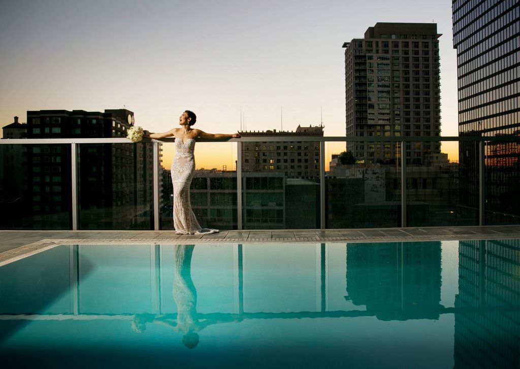 A downtown Los Angeles Bride is standing on a balcony overlooking a swimming pool.