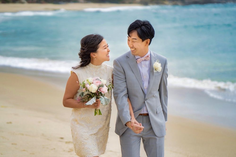 A bride and groom are walking on the beach holding hands in Laguna, California.