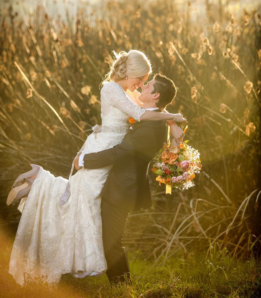 A bride and groom are kissing in a field of tall grass.
