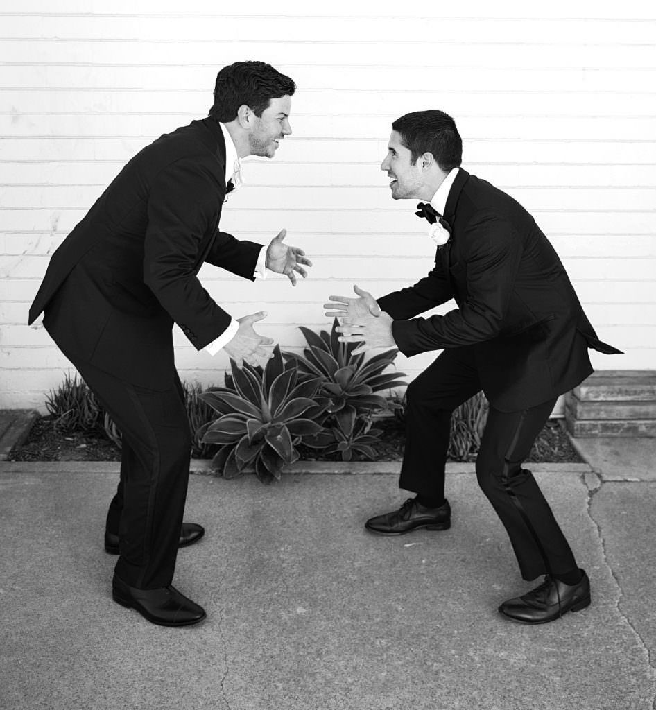 Two groomsmen are wrestling in tuxedos are standing next to each other