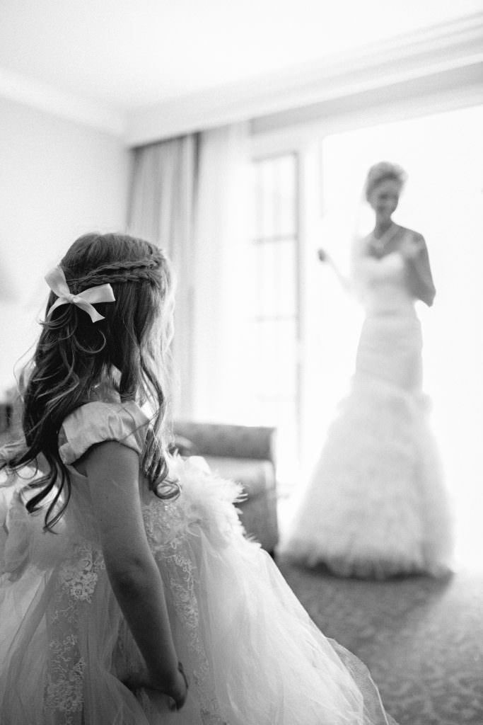 A flower girl is standing in front of a bride in a wedding dress.